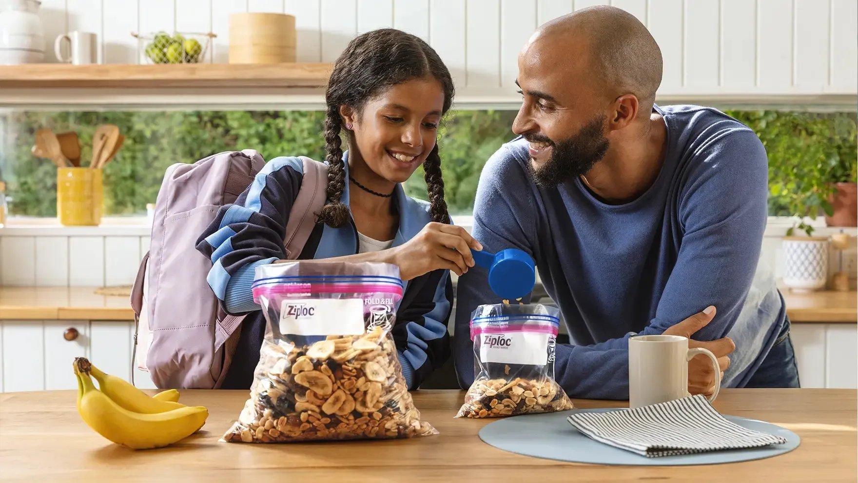 Father and daughter adding trail mix from a Large Ziploc® bag into a Medium Ziploc® bag